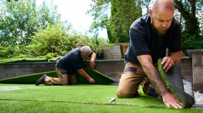 two workers installing artificial grass in home garden
